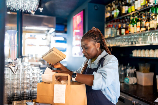 Female restaurant worker preparing take out food at checkout counter