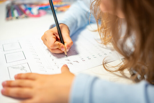 First grade girl practices handwriting with pencil in school workbook. Child learns to write letters during early education with selective focus and shallow depth of field