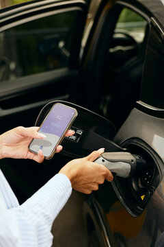 Hand of woman using mobile app while charging electric car