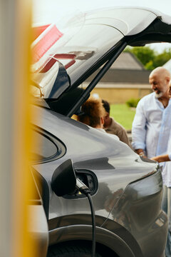 Electric plug connected in charging port of open car trunk at backyard