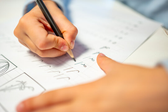 First grade student practices writing letters with pencil in workbook. Early literacy and handwriting skills develop with selective focus and shallow depth of field