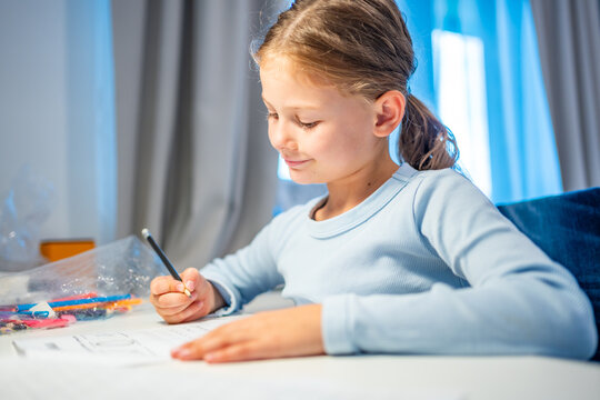 First grade girl writes with pencil while studying at home. Focused child develops handwriting and learning skills with selective focus and shallow depth of field