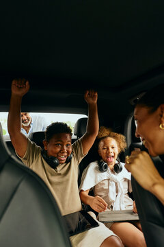 Cheerful siblings getting hyped up for their family summer trip while sitting in car