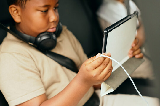 Boy charging tablet PC while cable charger while sitting in car during road trip