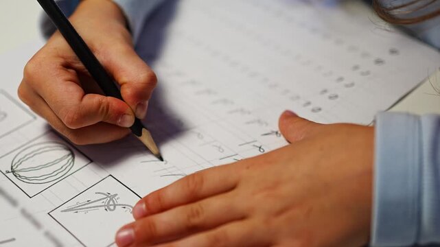 First grade student practices writing letters with pencil in workbook. Early literacy and handwriting skills develop with selective focus and shallow depth of field