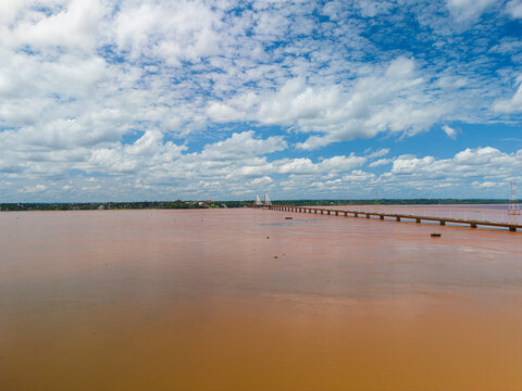 Aerial view of the San Roque Gonzalez de Santa Cruz Bridge spanning the wide Parana River under a bright blue sky with scattered clouds in Posadas, Misiones Province, Argentina.