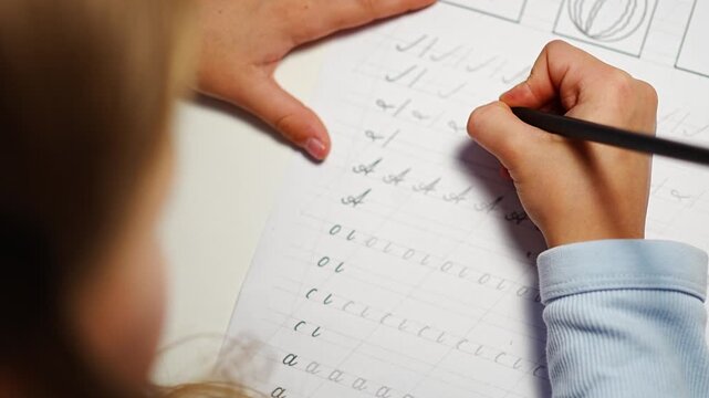 First grade girl practices handwriting with pencil in school workbook. Child learns to write letters during early education with selective focus and shallow depth of field
