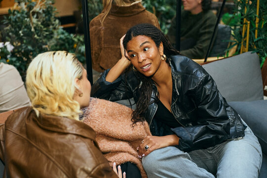 Young woman discussing with female friend while relaxing on sofa in greenhouse