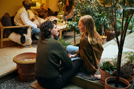 Young man spending leisure time with female friend while sitting on deck in courtyard