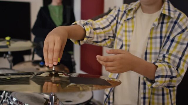 Caucasian teenage drummer assembling cymbal on drum kit stand during band rehearsal with guitarist. Footage suits music school advertising or youth hobby tutorials