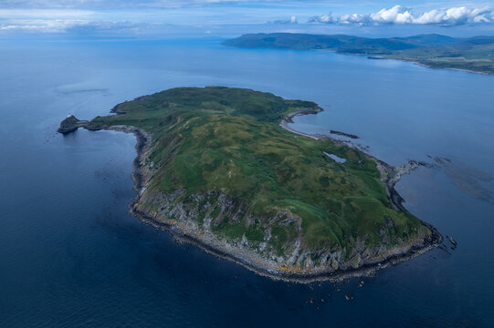 Aerial view of Sanda Island near the Mull of Kintyre, featuring rugged green terrain, rocky cliffs, a lighthouse, and surrounding deep blue waters, Argyll and Bute, Scotland, United Kingdom.