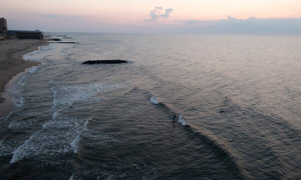 Aerial view of Asbury Park Beach at sunset with gentle waves rolling onto the sandy shore and a surfer in the water, Asbury Park, New Jersey, United States.