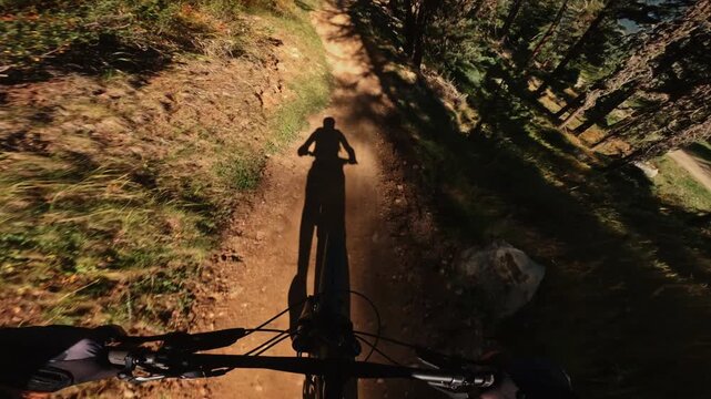 First-person POV footage of a mountain biker speeding downhill through a forest trail while following another cyclist, capturing fast movement, natural terrain and immersive outdoor action.