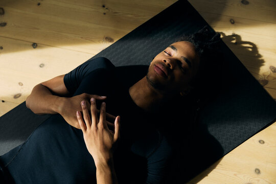 High angle view of young man meditating while lying on yoga mat at home