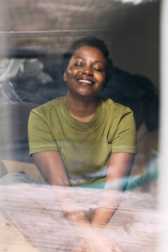 Happy woman relaxing while sitting at home seen through glass