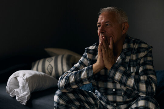 Depressed elderly man contemplating while sitting in bedroom