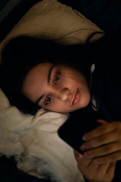 High angle view of teenage girl using her phone in bed at night