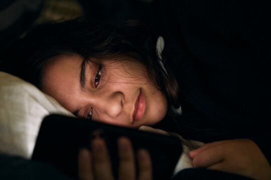 Close-up shot of teenage girl scrolling smart phone while lying in bed