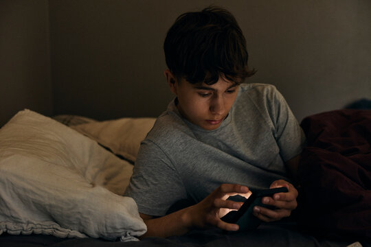 Teenage boy using smart phone during bedtime at home