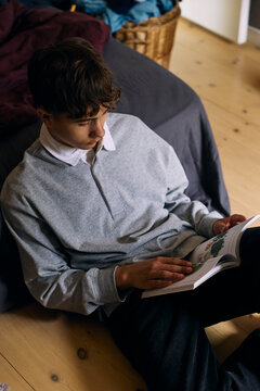 High angle view of teenage boy reading book while sitting at home