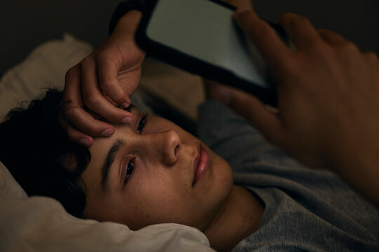 Close-up shot of anxious teenage boy using smart phone during bedtime