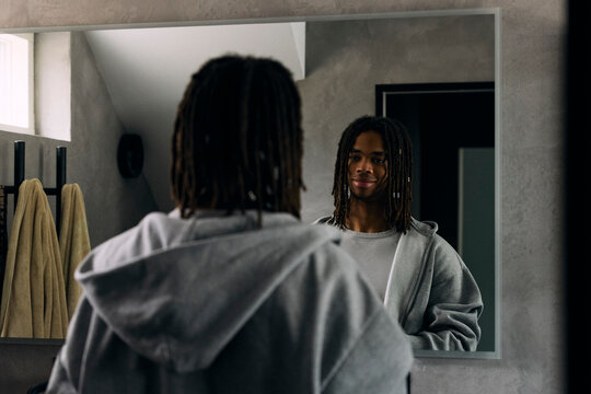 Smiling young man looking at his reflection in bathroom mirror