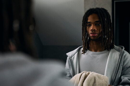 Young man holding towel and looking at his reflection in bathroom mirror