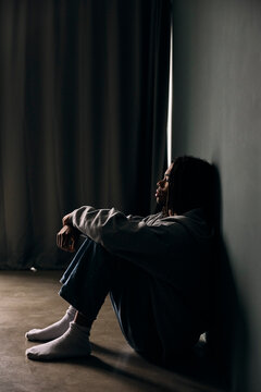 Full length of depressed young man sitting with eyes closed by wall at home