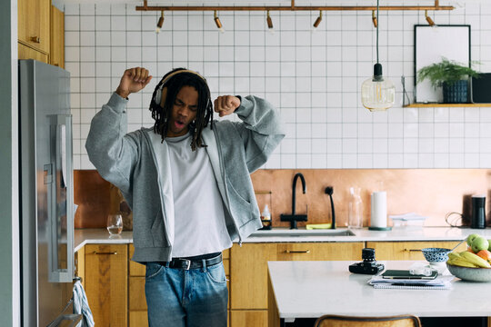 Carefree young man listening to music and singing in kitchen at home