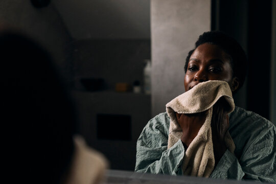 Woman wiping her face with towel while looking in bathroom mirror