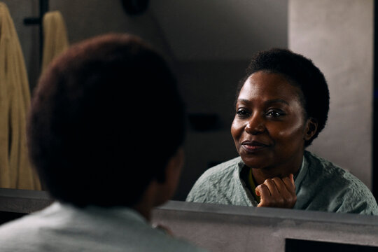 Smiling woman looking at her face in bathroom mirror