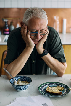 Stressed senior man looking at breakfast with loss of appetite
