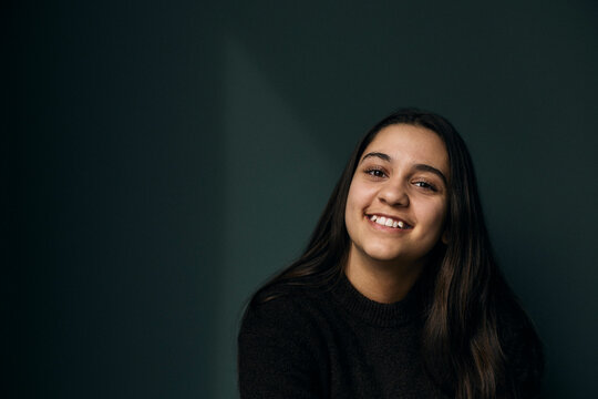 Portrait of happy teenage girl with long hair against wall