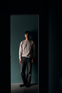Full length portrait of teenage boy standing against wall seen through doorway