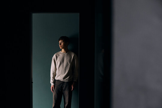 Worried teenage boy looking away while leaning on wall