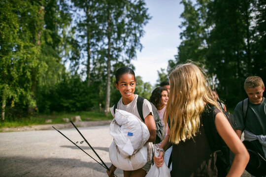 Girls holding camping gear and talking to each other while walking with friends at summer camp