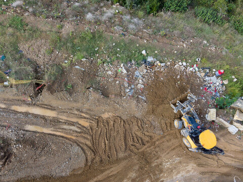 Aerial view of a yellow backhoe loader working on a muddy construction site with visible tire tracks and scattered debris in Istanbul, Istanbul, Turkiye.