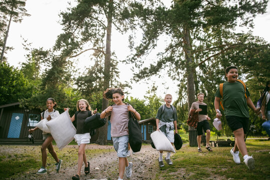 Group of excited children running on dirt path with their counselors at summer camp