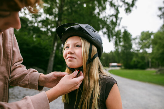 Female counselor assisting girl in wearing cycling helmet at summer camp