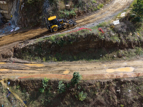 Aerial view of a yellow backhoe loader working on a muddy construction site with tire tracks and orange safety fencing Istanbul, Istanbul, Turkiye.