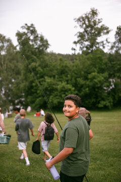 Portrait of boy looking over shoulder while walking on grass holding fishing rod at summer camp