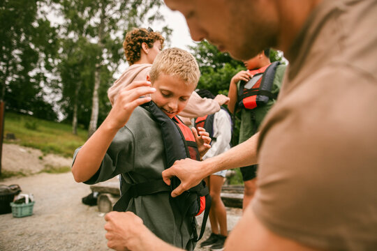 Boy with blond hair getting his life vest adjusted by camp leader
