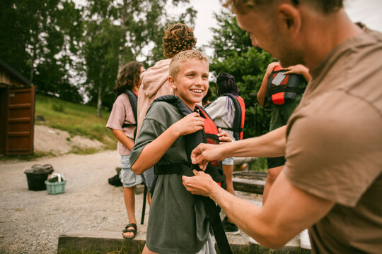 Smiling boy looking at male camp leader while wearing life jacket for outdoor activity