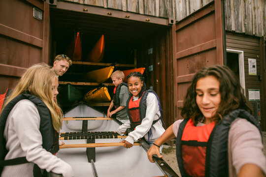 Group of happy children moving canoe out of storage container at summer camp
