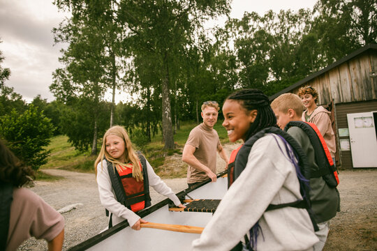 Group of happy children and their counselors carrying canoe at summer camp