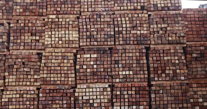 Background of neatly stacked square wooden beams in a lumberyard, wood factory. Close up of texture and ends of sawn timber blocks arranged in bundles. Rows of square cut wood planks stacked.