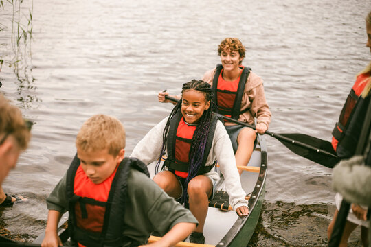 Smiling girl sitting in canoe with friends at summer camp