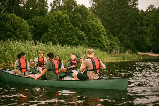 Counselors guiding group of kids during outdoor canoeing activity in lake at summer camp