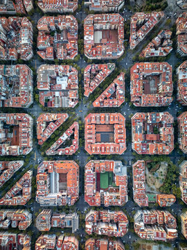 Aerial view of the iconic grid-patterned city blocks with chamfered corners and red-tiled roofs in the Eixample district of Barcelona, Catalonia, Spain.