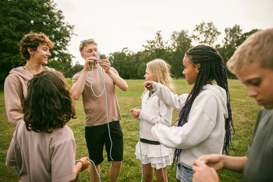Instructors teaching group of children to tie knot with rope on grassy field at summer camp